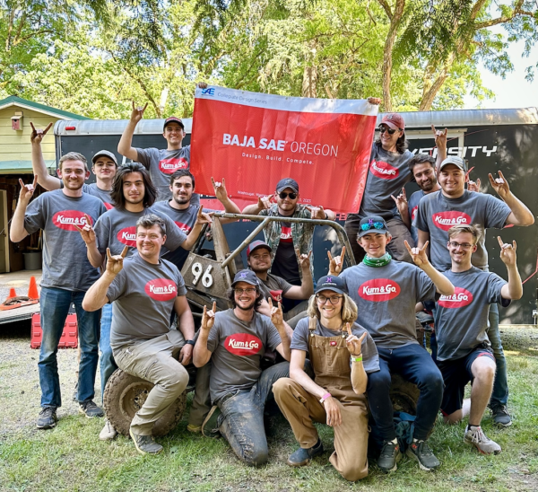 The NC State University Pack Motorsports Baja SAE Team poses for a group photo while holding aloft a red flag imprinted with BAJA SAE Oregon in white letters.