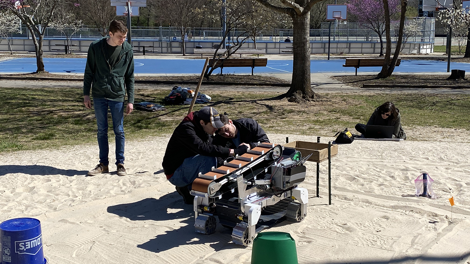 NC State mechatronics students work on a robot while outdoors in a sandlot.