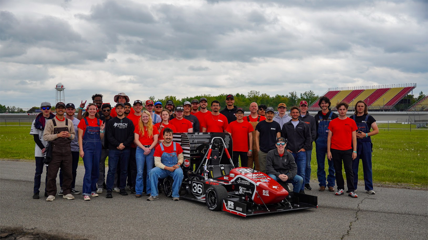 The Formula SAE team poses at a racetrack with the car they built.